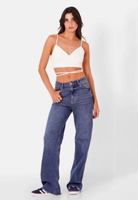 Top corto bianco a coste con spalline sottili abbinato a jeans larghi blu, con vita alta e un classico design a cinque tasche.