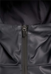 Acercamiento a una cremallera de chaqueta negra con un símbolo de calavera y huesos cruzados en la pestaña de la cremallera.