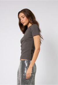 Szary, prążkowany top z krótkim rękawem o dopasowanym fasonie. Noszony z błyszczącą spódnicą wysadzaną srebrnymi cekinami sięgającą podłogi. Widok z boku.