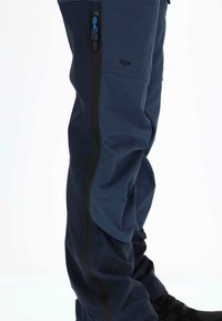 Granatowe spodnie sportowe o smukłym kroju, z czarnymi zamkami błyskawicznymi i bocznymi akcentami, wykonane z gładkiego, elastycznego materiału.