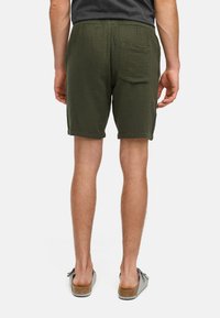 Menns olivengrønne shorts med teksturert stoff, elastisk midje og en enkelt baklomme, kombinert med grå slip-on sko.