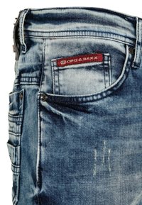 Denim jeans in een lichtblauwe wassing hebben een rood en wit label, meerdere zakken en subtiele verwerkte details aan de voorkant.
