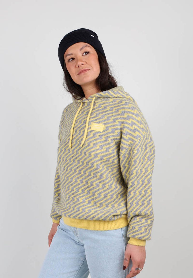 Haut à capuche à motifs gris et jaunes avec un design en zigzag, équipé d'une poche kangourou, de poignets côtelés et d'une capuche avec cordon de serrage.