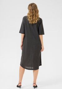Robe en lin gris foncé à coupe ample, manches courtes et fentes latérales, atteignant le milieu du mollet, avec un design simple et minimaliste.