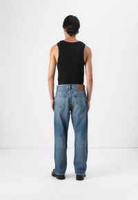 Zwarte mouwloze tanktop en blauwe rechte jeans met een bruine leren patch op de achterste tailleband. Soepele denimtextuur, comfortabele pasvorm.