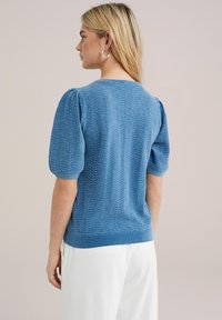 Suéter azul de punto con mangas cortas abullonadas, que presenta un patrón de zigzag texturizado y un cuello redondo. El dobladillo es acanalado para un ajuste ceñido.