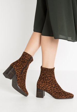 Kvinde iført brune ankelstøvler med leopardprint, blokhæle og sidelommer, kombineret med et mørkt, flydende skørt.