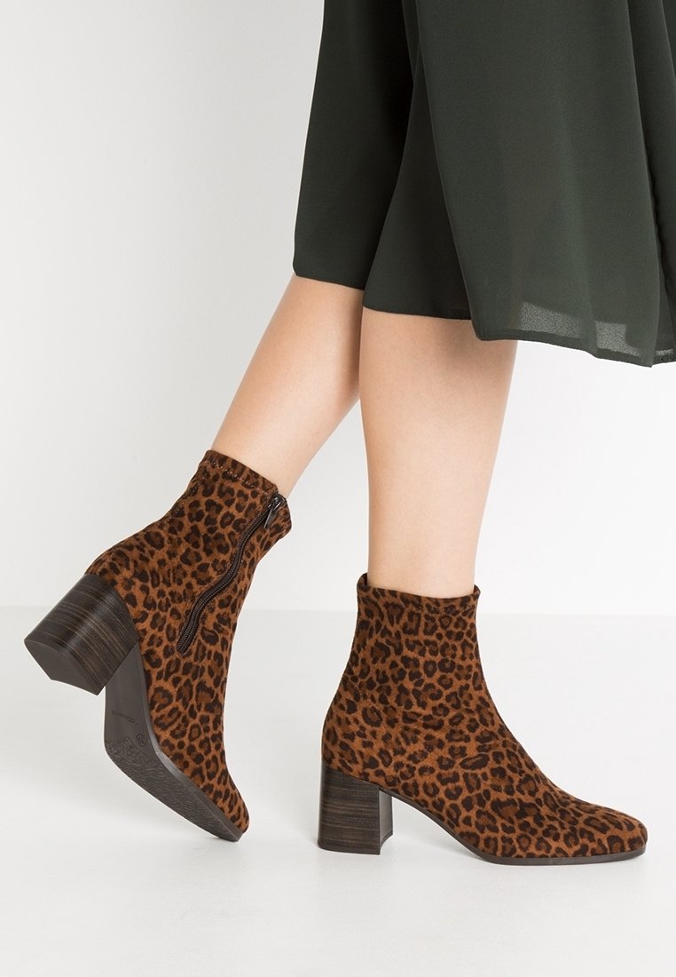 Femme portant des bottines marron à imprimé léopard, talons blocs et fermetures éclair latérales, associées à une jupe fluide foncée.