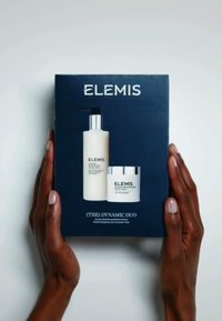 Le set Dynamic Duo d'Elemis dans une boîte bleu marine, comprenant une bouteille claire avec un bouchon pompe et un petit pot blanc, tous deux avec des accents en argent.