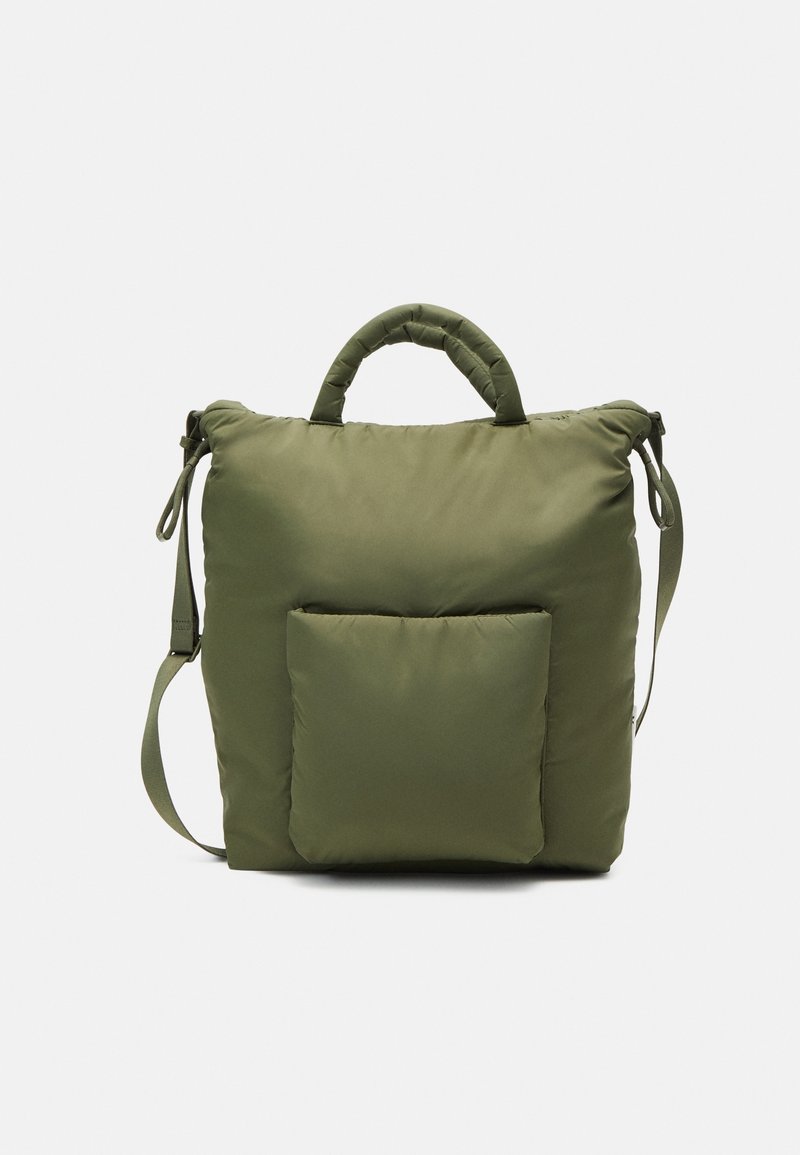 Sac carré matelassé vert olive avec poignée supérieure, poche zippée à l'avant et bandoulière ajustable sur fond uni.