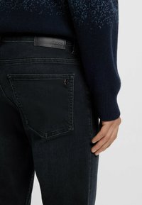 Jeans de mezclilla oscura con bolsillos traseros, parche de cuero en la cinturilla y detalle de puños acanalados en el suéter.