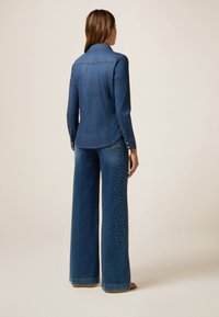 Giacca di jeans e jeans a gamba larga. Giacca: blu scuro, con colletto, design aderente. Jeans: blu scuro, decorati con borchie lungo i lati.