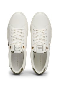 Hvite lær sneakers med en glatt overflate, som har gullfarge detaljer, runde snørebånd, og en kontrasterende olivengrønn såledetalj.