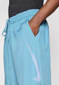 Light blue athletic shorts made of smooth fabric, featuring an elastic waistband with drawstring and a diagonal white striped pattern.