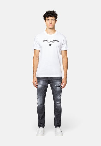 Witte katoenen T-shirt met zwart "DOLCE & GABBANA" logo, gecombineerd met versleten donkergrijze jeans en witte sneakers.