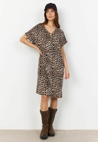 Leopardenmuster Kleid mit V-Ausschnitt und lockeren Ärmeln, aus weichem Stoff gefertigt. Kombiniert mit braunen kniehohen Stiefeln und einer schwarzen Mütze.