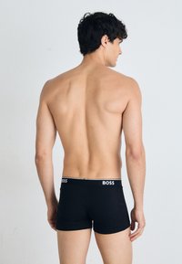 Schwarze Boxershorts aus glattem Material mit einem weißen Logo-Bund. Das Design ist figurbetont und zeigt eine klare Form mit minimalen Details.