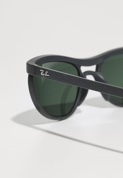 Lunettes de soleil Ray-Ban noires avec verres verts, finition mate lisse, forme élégante et petit logo en argent sur la branche extérieure.