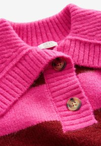 Gebreide polo trui met een geribbelde roze kraag, voorzien van een bruine ruitpatroon. Twee ronde knopen op de kraag voegen detail toe.
