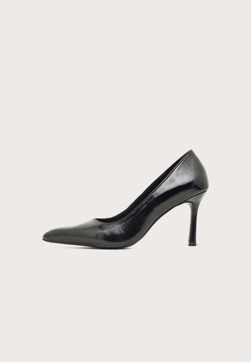 Chaussure à talon haut pour femme en cuir verni noir avec bout pointu et talon fin sur fond clair uni.