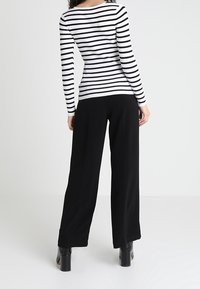 Pantalon noir à jambes larges associé à un haut à manches longues rayé noir et blanc côtelé. La tenue présente un col arrondi et un tissu texturé.