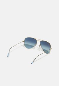 Ochelari de soare aviator cu ramă aurie și lentile gradiant în nuanțe de albastru. Bratele din metal au accente de albastru deschis. Pernuțele nazale transparente asigură confort.