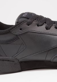 Baskets noires en cuir lisse avec des accents en tissu texturé. Elles présentent une languette en mesh, des lacets ronds et une semelle en caoutchouc plate.