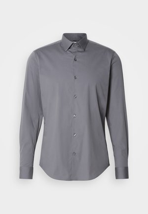 Pelēks garās piedurknes pogājams krekls, izgatavots no gludas kokvilnas. Tam ir klasiskā tipa apkakle un noapaļota apmale, kā arī sešas tumšas pogas priekšpusē.