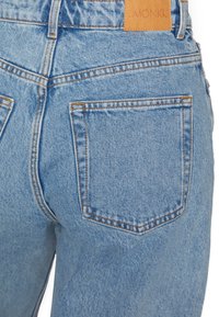 Ljusblå denimjeans med hög midja, två bakfickor och brun läderlapp med "MONKI"-logotyp. Framträdande sömnadsdetaljer.
