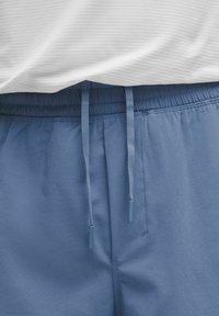 Heledad sinine lühikesed püksid, millel on elastne vöökoht, stringiga ja pehme tekstuur. Üks osa valgest soonilisest topist on osaliselt nähtaval.