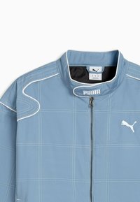 Lichtblauwe jas met hoge kraag, witte stiksels en PUMA-logo. Het materiaal lijkt glad met een subtiel ruitpatroon.