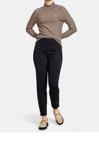 Randig polotröja i beige och brunt, kombinerad med svarta skräddarsydda byxor och beige loafers med detaljer av guldkedja.