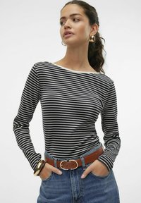 Zwart-wit gestreepte lange mouwtop, met een bootnek, gecombineerd met high-waisted blauwe jeans en een bruine riem met een gouden gesp.