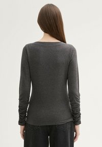 Maglia grigia a maniche lunghe realizzata in un tessuto morbido, con scollo rotondo e dettagli arricciati sulle maniche, abbinata a pantaloni scuri.