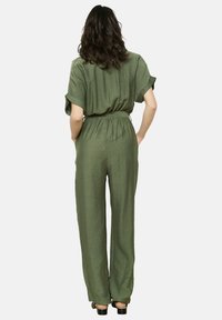Mono de color verde oliva con mangas cortas enrolladas, cintura ceñida, pantalones de pierna ancha y un acabado de tejido texturizado.