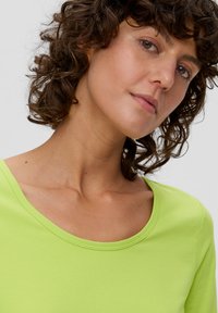 Limoengroene, korte mouwen, ronde hals t-shirt van zacht materiaal; close-up toont de textuur van het oppervlak en de gladde stiksels langs de halslijn.