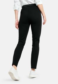 Zwarte, slim-fit broeken met een gladde textuur, enkel-lang ontwerp en een taille met ceintuur. Gepaard met witte sneakers.