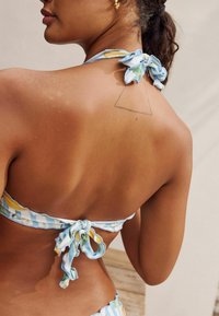 Multicolore bikini-top in een gestreept design met een strik op de rug. Zachte stof met bloemmotieven. Huid toont zongebruinde tinten en een tatoeage.