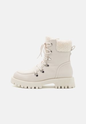 Botte d'hiver lacée de couleur crème avec semelle épaisse et détail en polaire au niveau du revers, conçue pour la chaleur et l'adhérence.