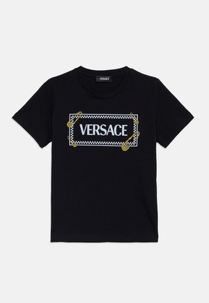 Melna kokvilnas T-kreklā ar baltu "VERSACE" logo, kas ietverts šaha laukuma rāmis, akcentēts ar zelta drošības adāmgaliem. Īsās piedurknes, parasts griezums.