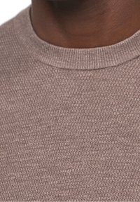 Grauer Strickpullover mit strukturiertem Muster, rundem Ausschnitt und gerippten Bündchen. Der Stoff wirkt weich und dick.