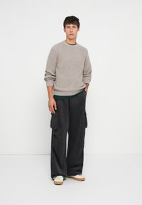 Maglione grigio lavorato a maglia con una texture a coste, abbinato a pantaloni cargo neri larghi con tasche laterali e sneakers beige.