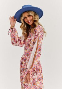 Květinové šaty v růžové, oranžové a modré barvě s dlouhými rukávy, které mají detaily vázání a boční výřezy; doplněné širokým modrým kloboukem.