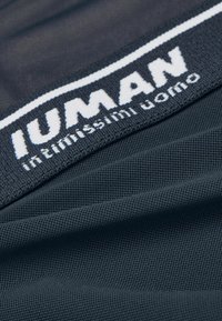 Ciemnoszara tkanina o teksturowanej powierzchni z czarną elastyczną opaską z napisem „IUMAN” w białych literach. Zawiera również tekst „intimo uomo”.