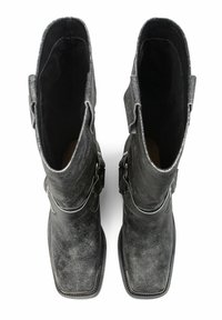 Par de botas de cuero negro de punta cuadrada con correas de hebilla metálica, vistas desde arriba sobre un fondo blanco.