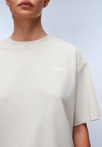 Beige bomulds t-shirt med en afslappet pasform, rund halsudskæring og korte ærmer. Har et subtilt hvidt logo på brystet.