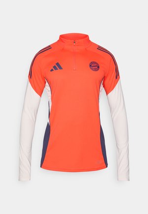 Camisola atlética vermelho-laranja com gola de fecho quarter-zip, mangas compridas brancas, detalhes em azul-marinho e três riscas pretas em cada ombro. Apresenta o logotipo da equipa.