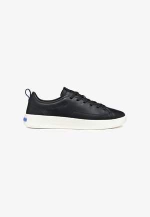 Black low-top sneaker with white sole, black laces, and a blue pull tab at the heel, shown from the outer side.