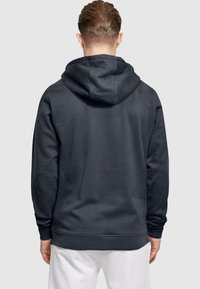 Mørkegrå hættetrøje med lange ærmer, en afslappet pasform og en tekstureret overflade. Enkel design uden synlige mønstre eller detaljer.