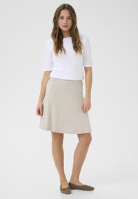 Beige utsvängd kjol med slät yta och elastisk midja, kombinerad med en figursydd vit topp. Ensemblen kompletteras av bruna ballerinaskor.